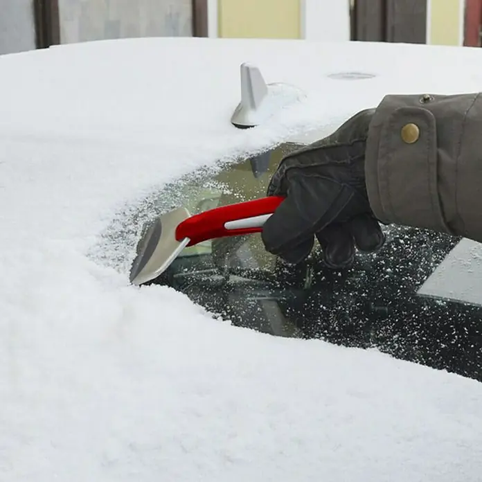 BAUHAUS Eiskratzer - Länge: 200 mm, Breite Schaberkante: 10 cm - Eine Hand mit Handschuh benutzt einen Eiskratzer mit rotem Griff, um Schnee von einer Autoscheibe zu entfernen.
