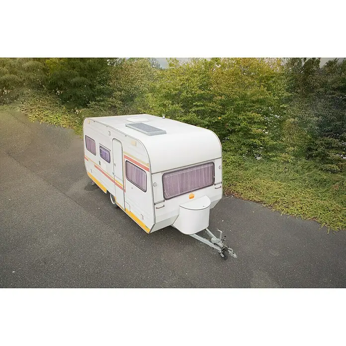 Sunset Solarmodul-Set Caravan - Nennleistung: 60 W, Für den Caravan- und Campingbereich - Ein weißer Wohnwagen steht auf einer Asphaltstraße, umgeben von üppigem Grün. Der Wohnwagen hat gelbe und orangefarbene Akzente und abgedunkelte Fenster.