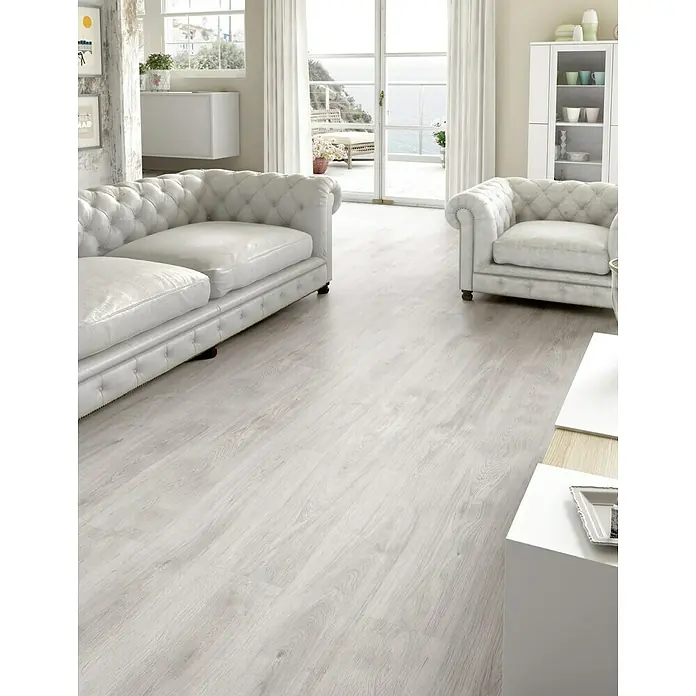 LOGOCLIC Laminado Roble Soho - 1.200 x 196 x 7 mm, Roble Soho, AC5 - Una sala de estar luminosa con muebles de cuero blanco y suelos de madera clara, creando un ambiente moderno y elegante.