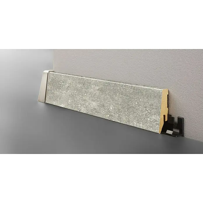 LOGOCLIC Sockelleiste K58 C Luzzi - 260 cm x 18 mm x 58 mm, MDF - Ein Sockelleisten-Element mit Steinmusterung und silberner Abschlusskappe, befestigt an einer grauen Wand.