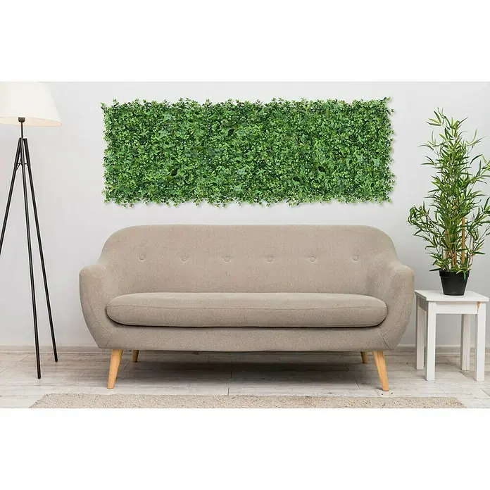 Faura Jardín vertical Mahonia - Plástico, L x An: 50 x 50 cm - Un sofá gris con un panel de pared verde con plantas encima, acentuado por una lámpara de pie y una planta en maceta en una mesa auxiliar.