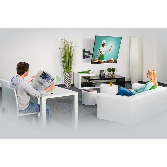 Hama Soporte para televisor Giratorio - Específico para: Diagonal de pantalla 32 - 65 pulgadas, Carga soportada: 25 kg - Una moderna escena de sala de estar con un soporte de pared para TV giratorio, mientras un hombre lee el periódico y una mujer mira la televisión.