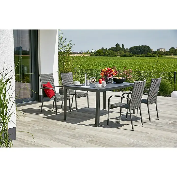 Gartenmöbel-Set Maja/Neila - 5 -tlg., Glas/Polyrattan/Aluminium/Stahl, Anthrazit/Silbergrau, Gartenstuhl stapelbar - Ein grauer Gartentisch mit vier Stühlen steht auf einer Terrasse, dekoriert mit Blumen und Geschirr. Perfekt für Mahlzeiten im Freien.