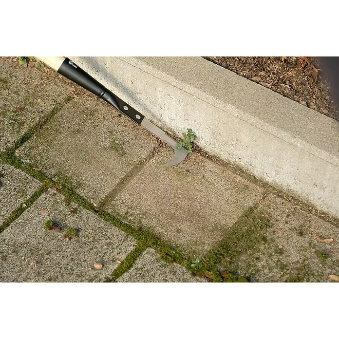Gardol Fugenkratzer - 135 cm - Nahaufnahme eines Fugenkratzers, der zwischen Pflastersteinen Unkraut entfernt. Das Werkzeug ist robust und ideal für die Gartenpflege.