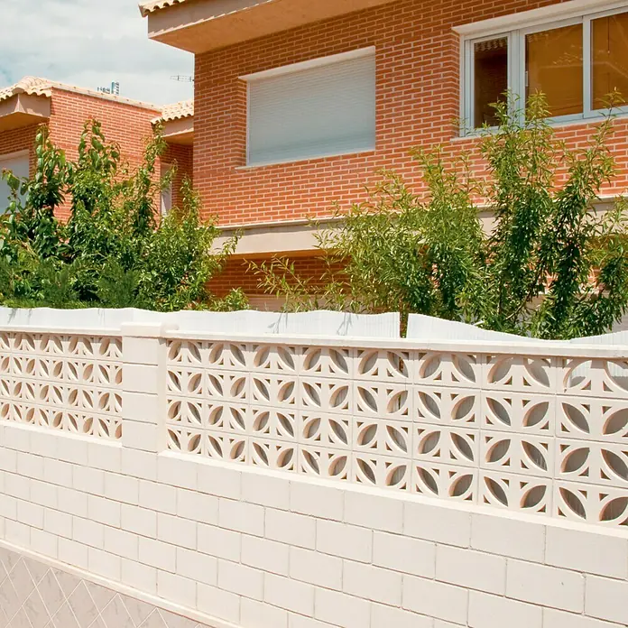 Celosía de pared Pétalos - 40 x 20 cm, Blanco - Primer plano de una valla decorativa de ladrillos con un patrón geométrico distintivo frente a un edificio residencial.