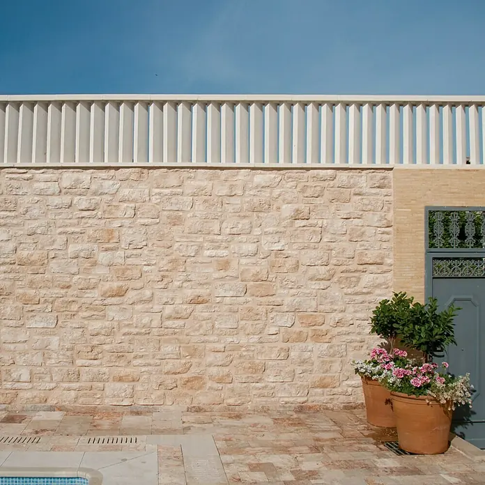 Protección contra el viento - Apto para: Ventilación - Pared de piedra con jardineras. La fachada de piedra natural bañada por el sol está acentuada por dos macetas de terracota plantadas y un cielo azul.