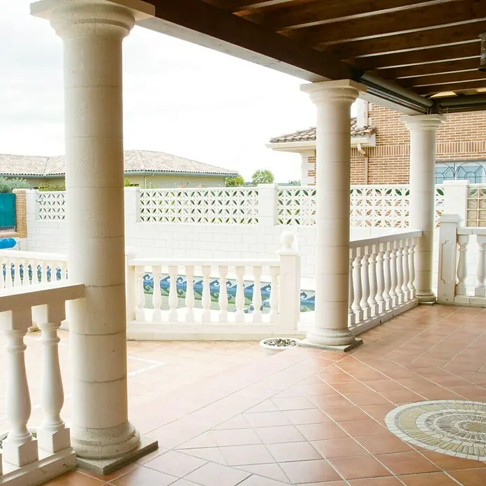 Columna decorativa Egeo - 25 x 30 cm, Blanco - Vista de una terraza con columnas, barandillas decorativas y baldosas rojas que crean un espacio exterior elegante y acogedor.