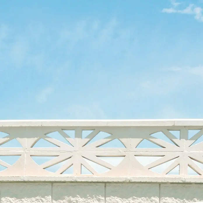 Celosía de pared Abanico - 40 x 20 cm, Blanco - Un primer plano detallado de una pared de ladrillos blanca, adornada con un patrón de celosía decorativo y calado. El cielo al fondo.\n