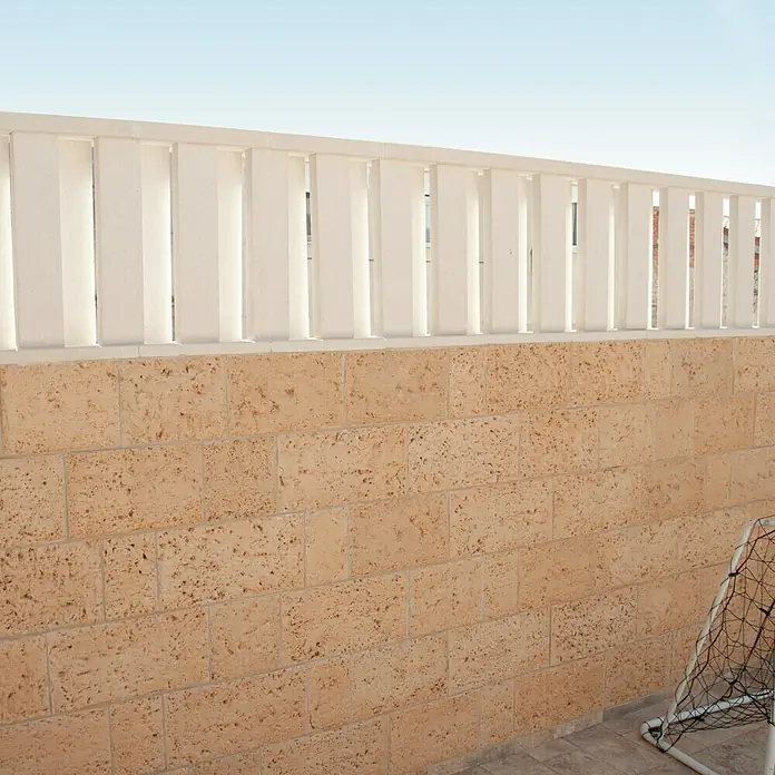 Tapa frontal de protección contra viento - Hormigón polímero, Blanco - Primer plano de una pared de piedra beige con una barandilla blanca encima, que muestra un estilo arquitectónico simple.