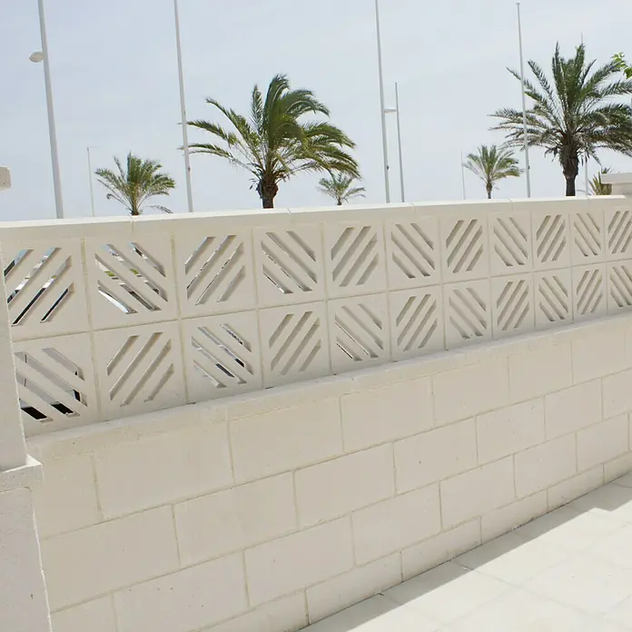 Celosía de pared Palmera - 25 x 25 cm, Blanco - Muro de ladrillo blanco con elementos cuadrados decorativos y palmeras al fondo, combinando textura con encanto tropical.