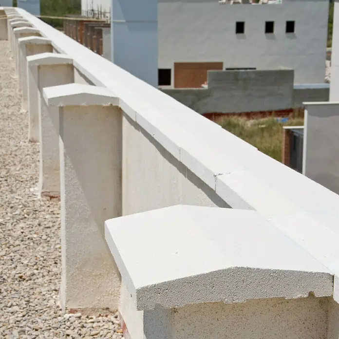 Cubremuros doble pendiente - 50 x 22 x 5 cm, Blanco, Hormigón - Primer plano de una pared de hormigón blanco con pilares y remates, proporcionando un acento arquitectónico limpio.