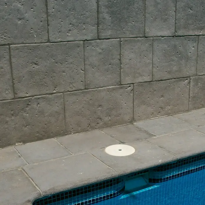 Pavimento para exterior Opus Roca - Gris - Primer plano de una piscina con azulejos de mosaico azules y azulejos de piedra gris que rodean la piscina. Una cubierta blanca es visible.