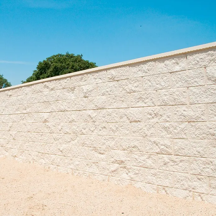 Bloque de hormigón poroso JM Split - 40 x 20 x 20 cm, Blanco - Primer plano de un muro de piedra robusto, diseñado como un edificio o estructura de contención robusta, con cielo azul y árboles verdes.