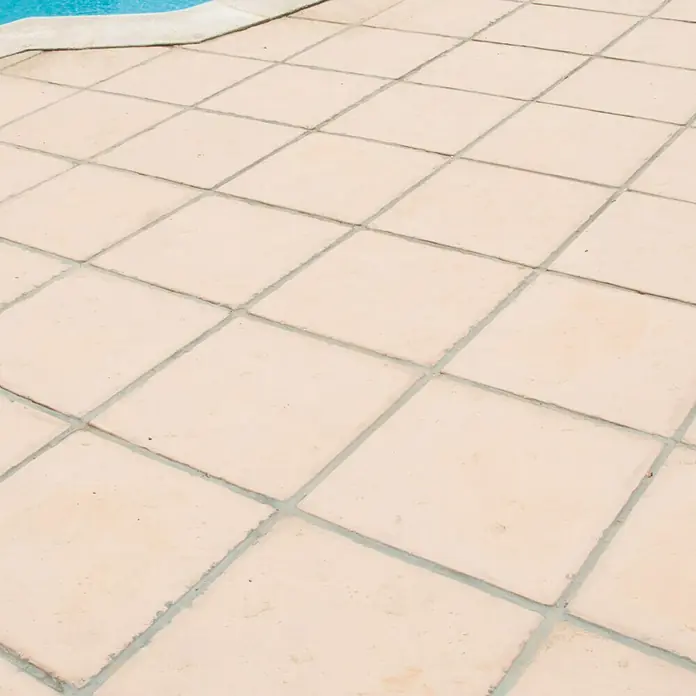 Pavimento para exterior Nerja - 50 x 50 cm, Ámbar - Primer plano de baldosas de terracota beige que rodean una piscina, con agua azul visible al fondo. Las baldosas están dispuestas en un patrón cuadrado.