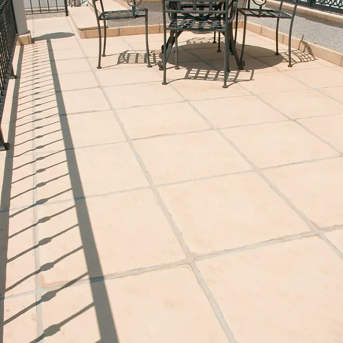 Pavimento para exterior Nerja - 50 x 50 cm, Ámbar - Imagen de una zona exterior con adoquines cuadrados y un juego de mesa de metal, creando un ambiente acogedor.