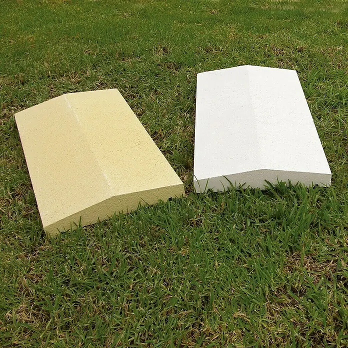 Cubremuros doble pendiente - 50 x 27 x 5 cm, Crema, Hormigón - Dos lápidas de piedra clara están colocadas sobre una superficie de hierba, una blanca y una amarilla. Destacan sobre la hierba verde.