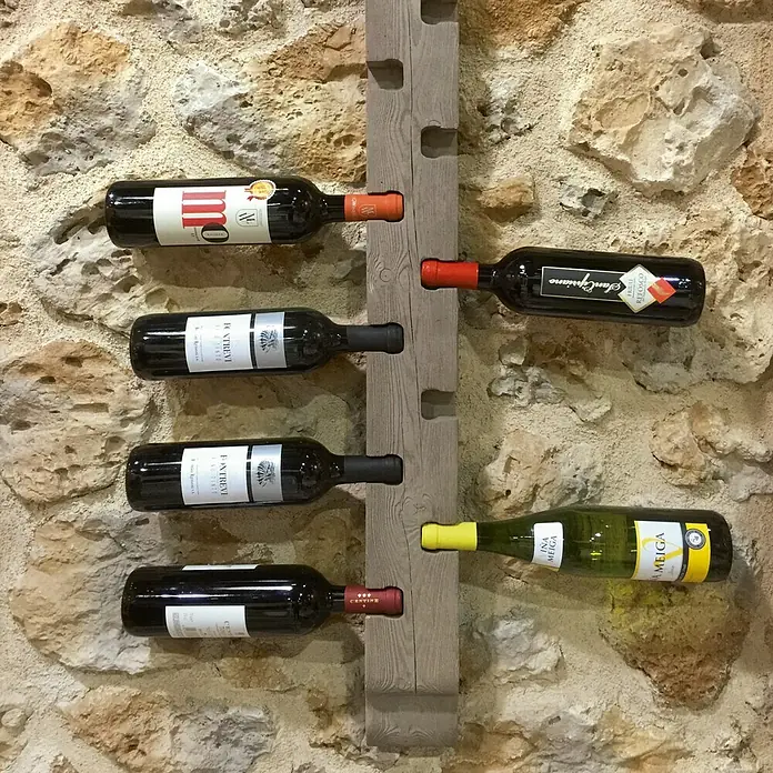 Estantería para botellas Nogal - 90 x 10 x 5,5 cm - Una vista de cerca de un botellero de madera con varias botellas de vino frente a una pared de piedra.