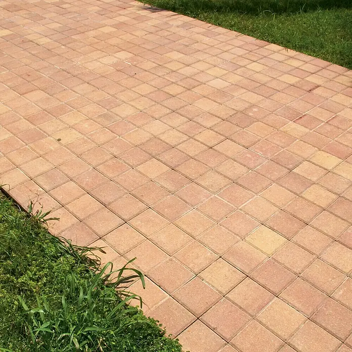 Loseta de exterior Irisada - 15 x 15 x 3,5 cm, Terracota, Hormigón - Primer plano de un camino pavimentado con adoquines cuadrados, bordeado de césped, creando un ambiente cálido y acogedor.