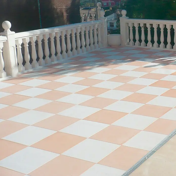 Pavimento para exterior Granulada - 50 x 50 cm, Salmone - Vista de una terraza con baldosas de damero y una balaustrada blanca, que muestra un diseño exterior elegante.