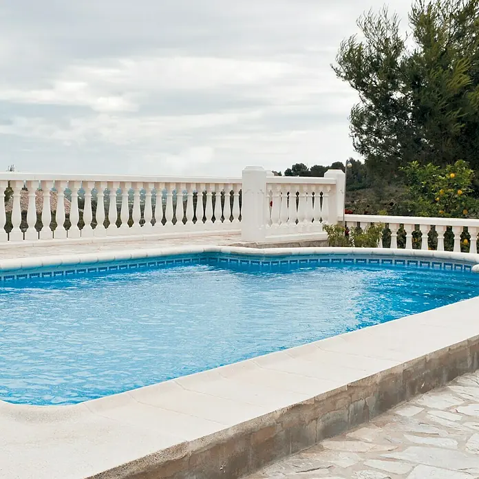 Pavimento remate Piscina R1 - 50 x 25 cm, Blanco - Atractiva área de piscina con agua turquesa, rodeada de una balaustrada blanca y vegetación exuberante. Ideal para relajarse y disfrutar.