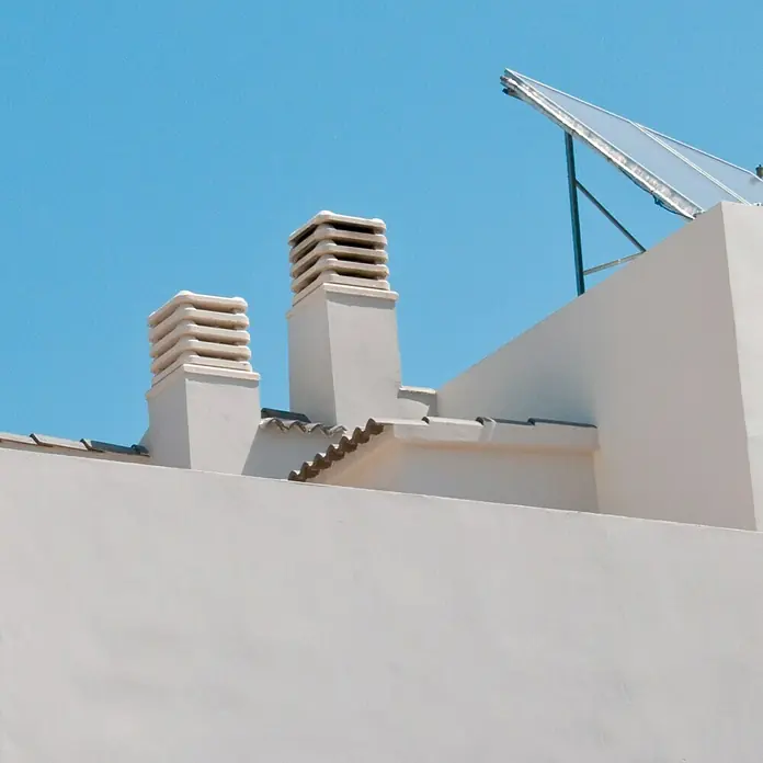 Aspirador estático 50 - Blanco - Primer plano de una azotea con dos chimeneas y una placa solar contra un cielo azul.