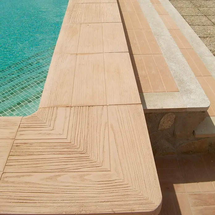 Placas para caminos inverso Teka 5.1 - 50 x 45 x 5 cm, Marrón, Hormigón - Primer plano de baldosas de piscina con apariencia de madera. Bordea una piscina con agua azul clara, brindando un toque natural y elegante.