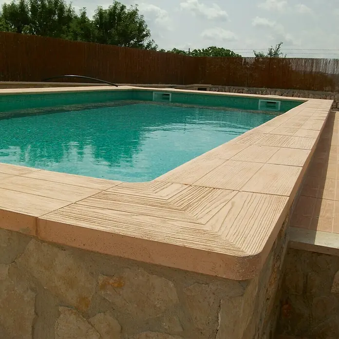 Placas para caminos inverso Teka 5.1 - 50 x 45 x 5 cm, Marrón, Hormigón - Primer plano de una piscina con agua turquesa y borde de piedra con aspecto de madera, que ofrece una vista acogedora en un día soleado.
