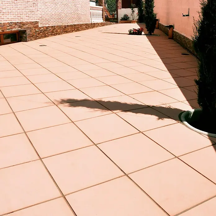 Pavimento para exterior Granulada - 50 x 50 cm, Salmone - Toma exterior que muestra baldosas cuadradas de terracota y sombras de árboles, destacando el diseño limpio y uniforme del espacio exterior.