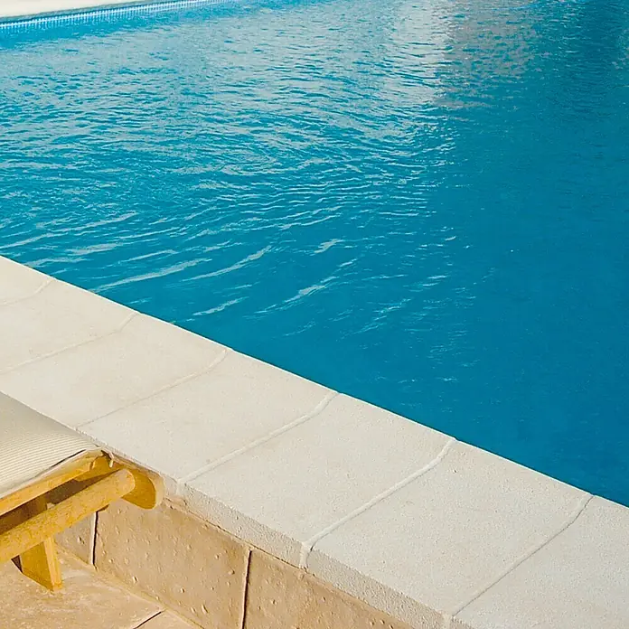 Pavimento remate Piscina R1 - 50 x 25 cm, Blanco - Primer plano de una piscina con agua azul y una cubierta de piscina de color claro, creando una transición limpia entre la piscina y la zona de descanso.