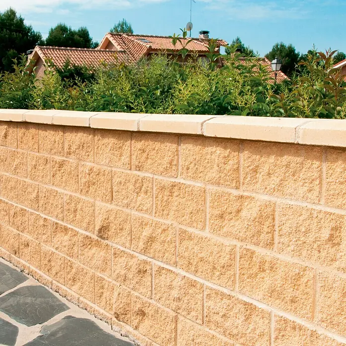 Bloque de hormigón poroso Split - 40 x 20 x 20 cm, Crema, Hormigón, Ligeramente irregular - Primer plano de un muro de piedra color arena con una coronación de piedra lisa, que sirve como límite exterior decorativo de la propiedad.