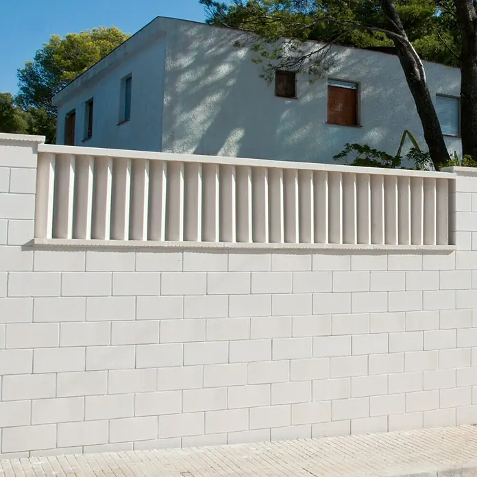 Bloque de hormigón poroso JM - 40 x 15 x 20 cm, Blanco, Hormigón - Una toma detallada de una pared de ladrillos blancos rematada con un diseño de cerca ornamentada, con un edificio visible al fondo.