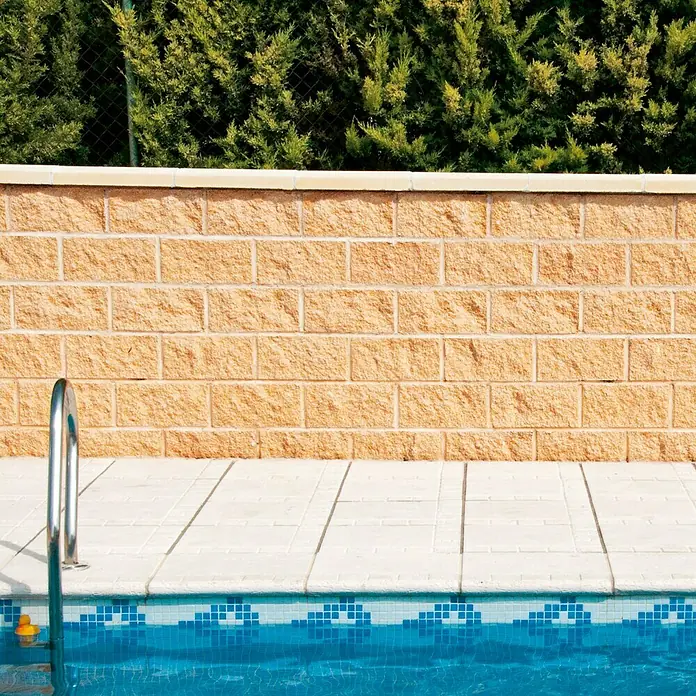 Bloque de hormigón poroso Split - 40 x 20 x 20 cm, Crema, Hormigón, Ligeramente irregular - Primer plano de una piscina con azulejos de mosaico azul y una escalera de acero inoxidable que conduce al agua.