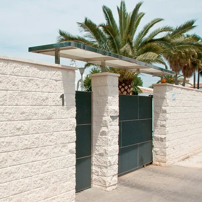 Bloque de hormigón poroso JM Split - 40 x 20 x 20 cm, Blanco - Una entrada moderna con una puerta de metal gris y un techo elegante frente a palmeras.
