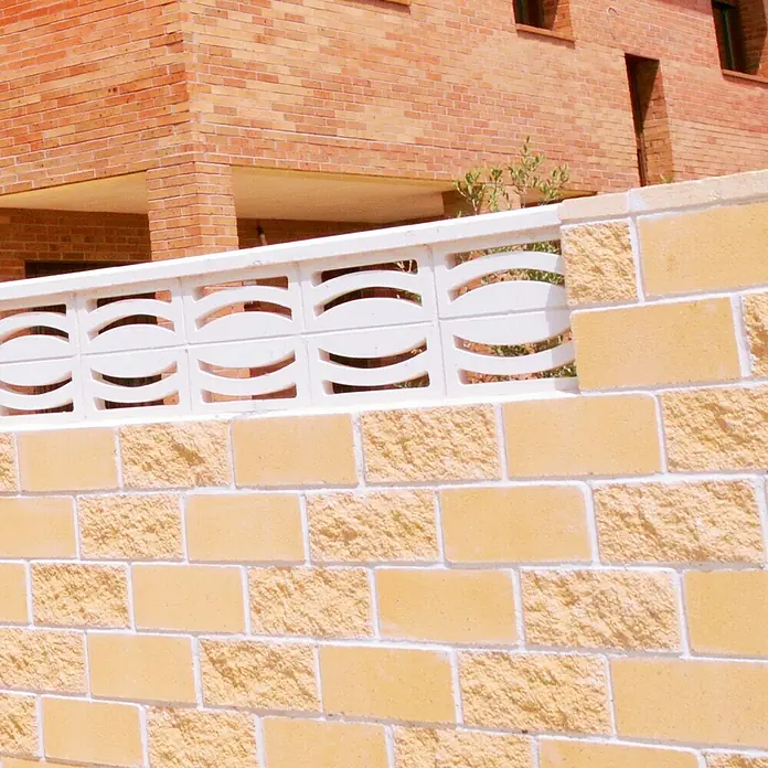 Bloque de hormigón poroso JM - 40 x 20 x 20 cm, Crema, Hormigón - Primer plano de una pared de ladrillos decorativa con detalles en blanco, resaltando textura y diseño.