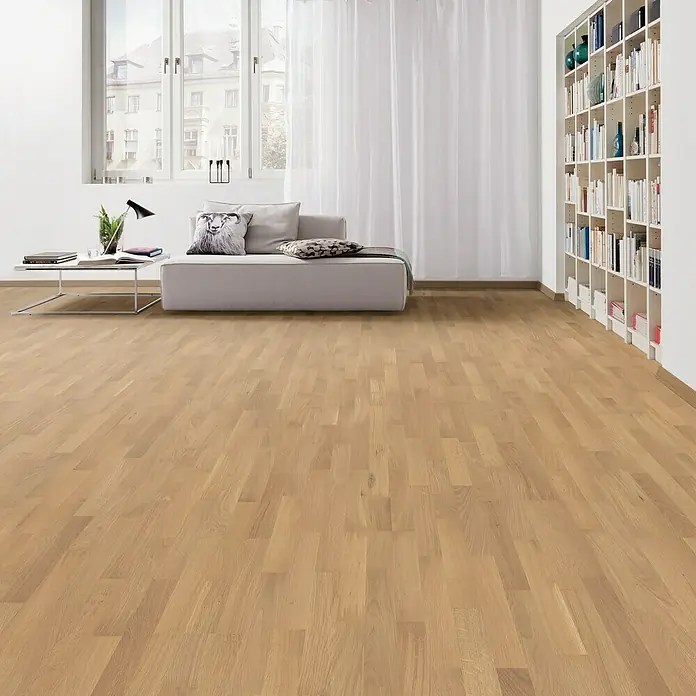 Living by Haro Parkettmuster Eiche Pure Naturöl - 290 x 180 x 12 mm, Schiffsboden - Heller Raum mit Parkettboden, Sofa, Bücherregal und Vorhängen. Der Fokus liegt auf dem warmen Holzton des Bodens.