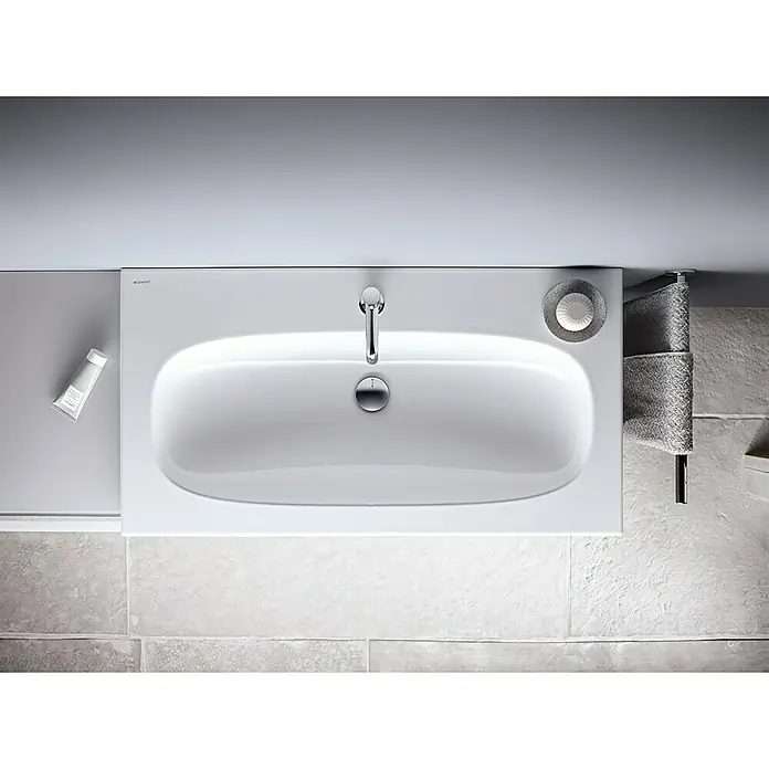 Geberit Acanto Waschtisch - 60 x 48 cm, Mit schmutzabweisender Glasur, Hahnloch: Mitte, Mit Überlauf, Weiß - Moderne Aufsicht auf ein weißes Waschbecken mit Armatur, Seife und einer Tube Creme, das eine stilvolle und funktionale Badezimmerlösung darstellt.