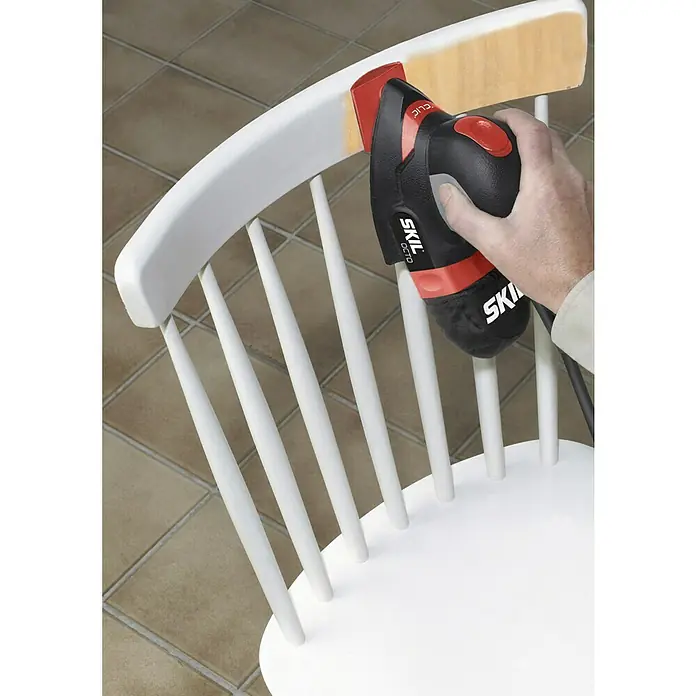 Skil Elektro-Multischleifer 7207 AA - 100 W, Leerlaufschwingzahl: 24.000 U/min, Durchmesser Schwingkreis: 1,6 mm - Nahaufnahme eines Mannes, der mit einem Skil-Oktoschleifer einen weißen Holzstuhl abschleift, um ihn zu restaurieren.