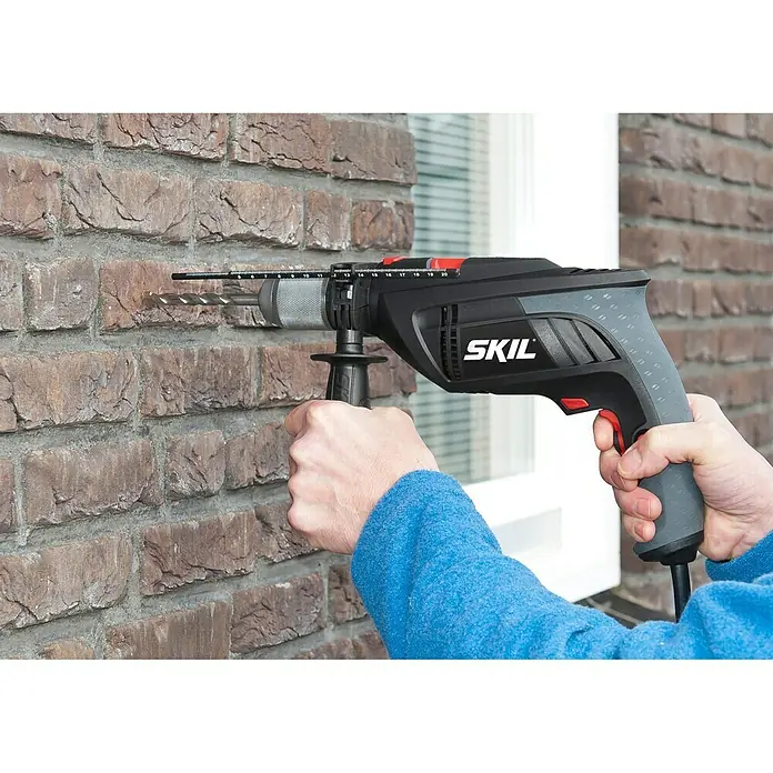 Skil Schlagbohrmaschine 6398 AA - 1.000 W, Schnellspannbohrfutter - Ein Bediener bohrt mit einer SKIL Bohrmaschine ein Loch in eine Ziegelwand. Die Bohrmaschine ist schwarz-grau mit roten Akzenten.