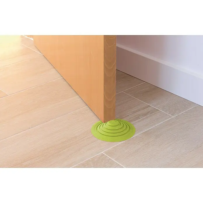 Tope de puerta y ventana Ovni Blockystar - Plástico, Ø x Al: 12 x 3 cm, Verde - Un tope de puerta de silicona verde en forma de disco mantiene una puerta abierta sobre un suelo de baldosas.