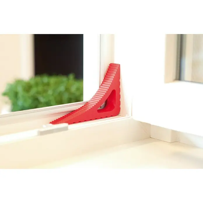 Retenedor para puerta y ventana Blockystar - Rojo - Cuña de ventana de plástico roja colocada en un marco de ventana blanco, lo que garantiza un fácil uso y una sujeción segura.
