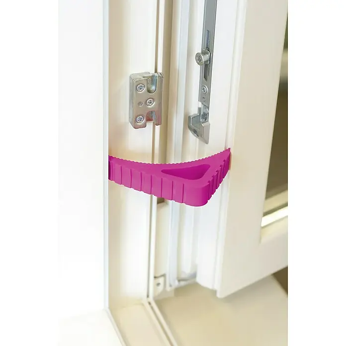 Retenedor para puerta y ventana Blockystar - Rosa - Primer plano de un tope de puerta rosa que mantiene una puerta abierta, con herrajes visibles en el marco blanco de la puerta.