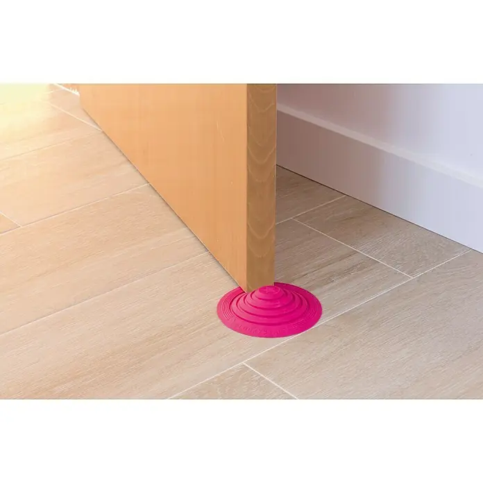 Tope de puerta y ventana Ovni Blockystar - Plástico, Ø x Al: 12 x 3 cm, Rosa - Un primer plano muestra un tope de puerta rosa que mantiene una puerta de madera abierta sobre un suelo de baldosas brillantes.