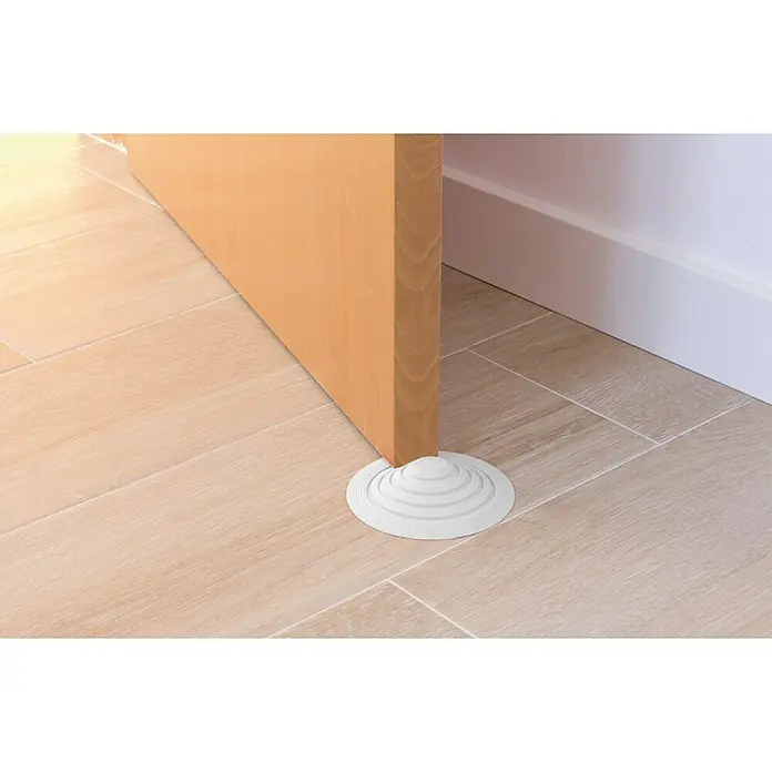 Tope de puerta y ventana Ovni Blockystar - Plástico, Ø x Al: 12 x 3 cm, Blanco - Un tope de puerta de goma sujeta una puerta de madera abierta sobre un piso de baldosas, evitando que se cierre de golpe.