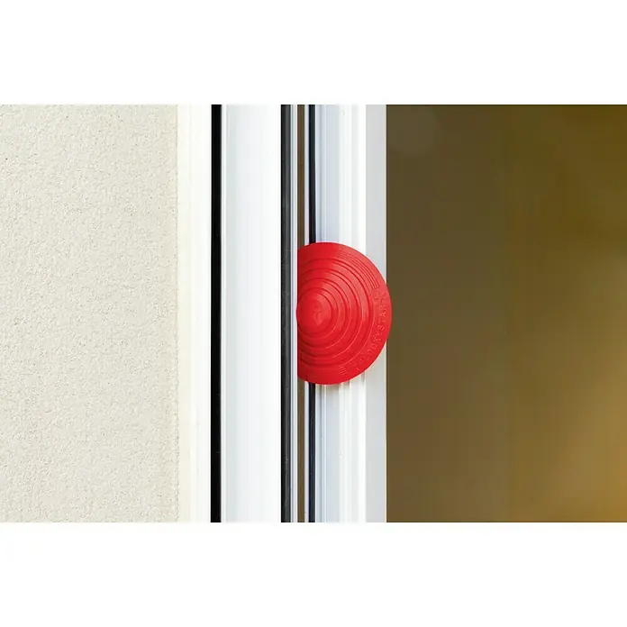 Tope de puerta y ventana Ovni Blockystar - Plástico, Ø x Al: 12 x 3 cm, Rojo - Imagen de un tope de puerta rojo encajado entre una puerta para mantenerla abierta.
