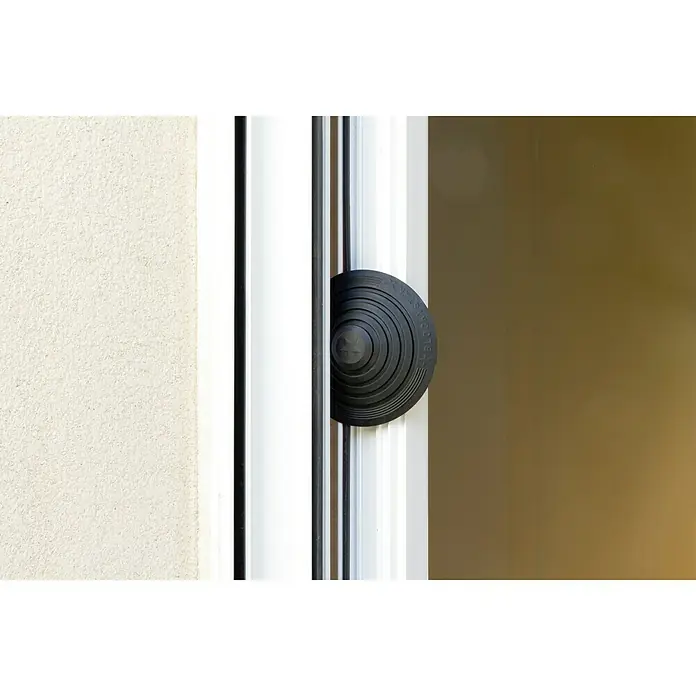 Tope de puerta y ventana Ovni Blockystar - Plástico, Ø x Al: 12 x 3 cm, Negro - Primer plano de un bloqueador de puerta Block Star negro y redondo en un marco de puerta blanco, para un hogar seguro y elegante.
