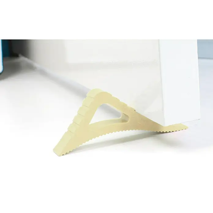 Retenedor para puerta y ventana Blockystar - Beige - Un tope de puerta triangular beige con bordes serrados mantiene una puerta blanca abierta sobre una superficie blanca.