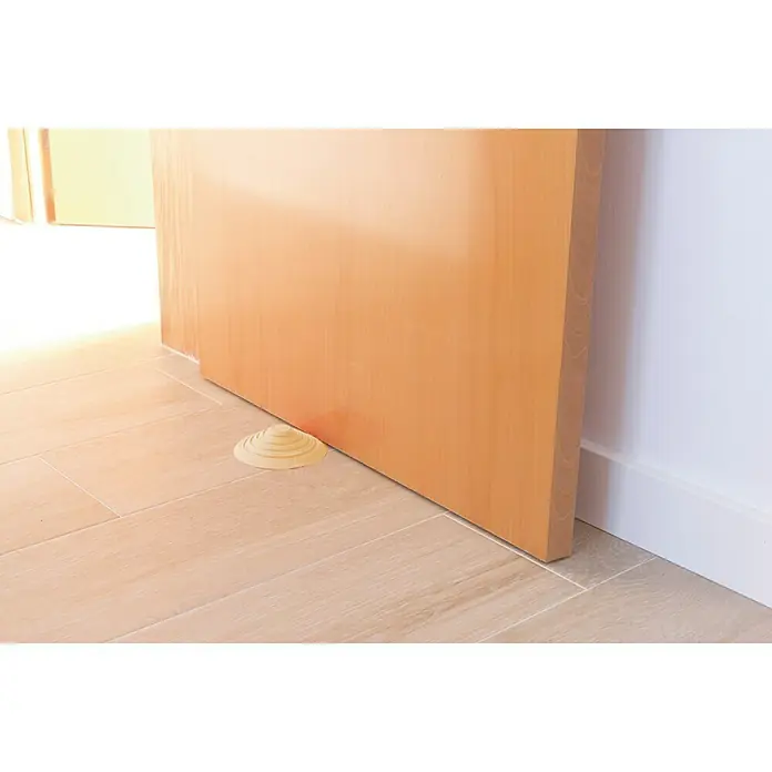 Tope de puerta y ventana Ovni Blockystar - Plástico, Ø x Al: 12 x 3 cm, Beige - Un tope de puerta beige en forma de cono mantiene una puerta de madera clara abierta sobre un piso de baldosas.