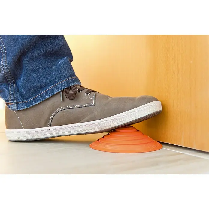 Tope de puerta y ventana Ovni Blockystar - Plástico, Ø x Al: 12 x 3 cm, Naranja - Un zapato gris sujetando un tope de puerta naranja en forma de cono, manteniendo la puerta abierta. Accesorio práctico para cualquier hogar.
