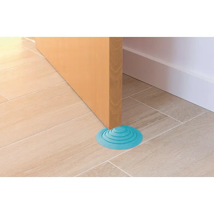 Tope de puerta y ventana Ovni Blockystar - Plástico, Ø x Al: 12 x 3 cm, Azul - Tope de puerta azul que mantiene una puerta de madera abierta sobre un suelo de baldosas. El tope de puerta tiene un diseño en espiral para un agarre seguro.