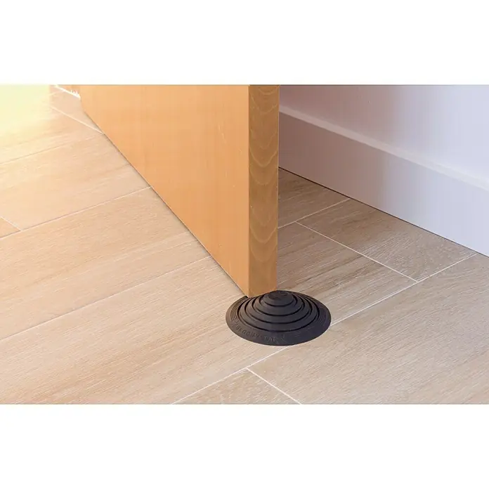 Tope de puerta y ventana Ovni Blockystar - Plástico, Ø x Al: 12 x 3 cm, Negro - Un tope de puerta cónico negro mantiene una puerta de madera abierta sobre un suelo de baldosas claras.